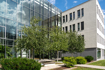 Modern Office Building In Munich Bavaria: Glass Facade Reflecting Sky And Clouds, White Concrete...