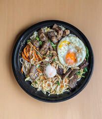 A top-down photo of a black round plate containing a colorful and detailed Korean-style bibimbap dish.