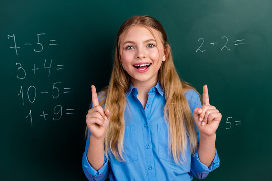 Smiling schoolgirl raising hands in a classroom with equations on a chalkboard, expressing learning and enthusiastic engagement - Powered by Adobe