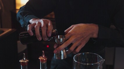 Cropped hand bartender using jigger measure pouring ingredients liquor syrup into mixing glass...