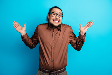 Young stylish man in brown formalwear making a humorous shrug gesture against a vibrant teal...