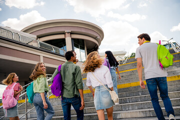 Group of cheerful students walking outdoor on a sunny day carrying backpacks at a modern urban...