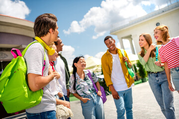 Group of cheerful young friends bonding outdoors during a sunny day, discussing and laughing in a...