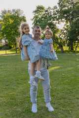 Fototapeta premium Dad holds his two daughters in his arms, a walk in the city park, family leisure time
