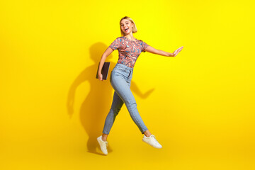 Attractive young woman joyfully jumping with a laptop against a vibrant yellow backdrop showcasing...