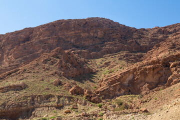 Rugged red rock hills under clear blue skies in Hormozgan, Iran, showcasing natural erosion patterns and sparse desert vegetation.