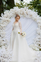 Elegant bride stands gracefully in a floral arch amidst a serene outdoor setting