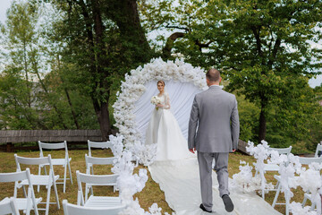 Couple walks towards floral archway during outdoor wedding ceremony in a lush garden setting