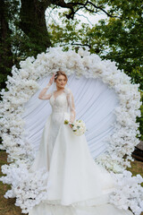 Elegant bride posing in floral arch during outdoor wedding ceremony celebration