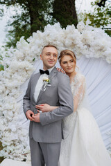 Couple poses together at wedding ceremony surrounded by floral decorations in outdoor setting
