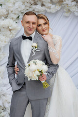 Newlywed couple poses happily in elegant wedding attire in a beautiful floral setting