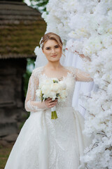 Bride poses gracefully beside floral backdrop in elegant wedding attire
