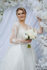 Beautiful bride posing with bouquet in floral backdrop during wedding celebration