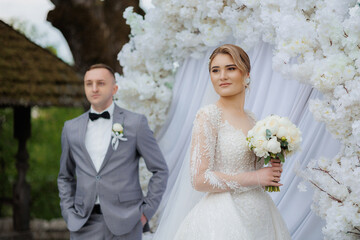 Elegant wedding couple posing by floral backdrop on a sunny day