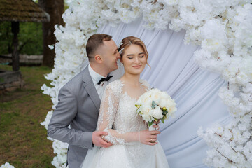 Romantic wedding couple posing in front of flowering backdrop in a serene outdoor setting