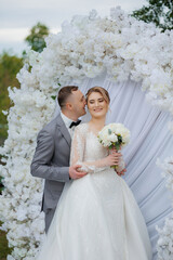 Couple embraces in romantic wedding setting surrounded by floral arch