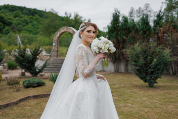 Bride in elegant dress holding bouquet in serene garden on cloudy day