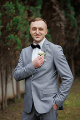 Groom posing elegantly in a gray suit with boutonniere outdoors