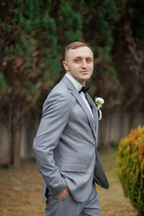 Groom in a gray suit poses elegantly in a garden during a wedding ceremony