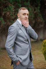 Stylish man in a grey suit poses thoughtfully in a serene outdoor setting