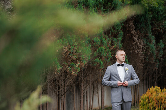 Groom adjusting his bow tie in a lush garden setting during a wedding celebration