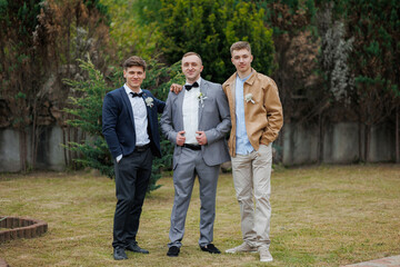 Three young men in formal attire posed together at a garden setting during a celebration