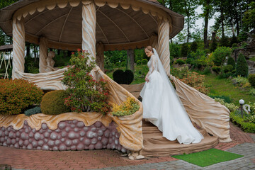 Bride ascending staircase in elegant garden gazebo during outdoor wedding ceremony preparation