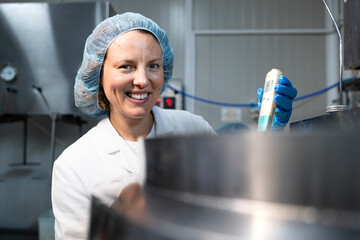 Female technologist in sterile clothing and hairnet checking PH value in food container.