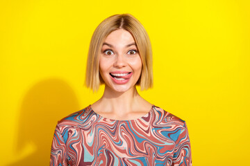 Portrait of a cheerful young woman in a colorful top making a funny face against a vibrant yellow...
