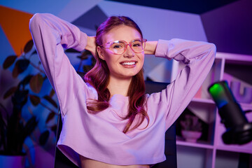 Young female blogger in casual sweatshirt posing in neon lit room with professional microphone for...