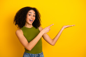 Joyful young woman in stylish casual outfit gesturing invitingly against vibrant yellow background