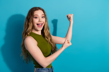 Cheerful young woman raising her fists in celebration against a vibrant blue background, showcasing...