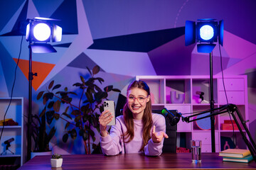 Podcaster woman recording live video content at home setup, involving vibrant lighting and...