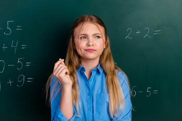 Young schoolgirl in a classroom contemplating math problems on a chalkboard, symbolizing education...