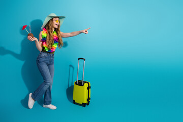 Young woman pointing in excitement wearing casual tropical outfit with hat holding drink cup...