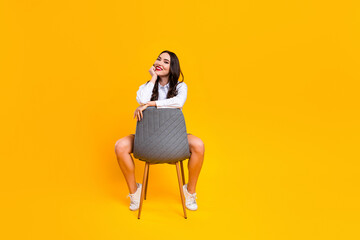 Charming woman sitting stylishly on a chair against a yellow background representing leisure,...
