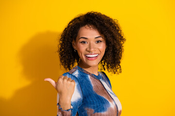 Young woman with curly hair wearing a colorful print top in front of a bright yellow background...