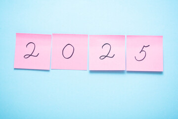Pink sticky notes spelling out the year 2025 against a bright blue background.