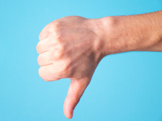 Close-up of a hand giving a thumbs-down gesture against a bright blue background.