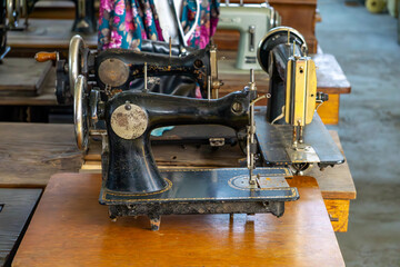 Vintage sewing machines arranged in a row on wooden tables. Old hand-powered tailoring devices displayed in a workshop