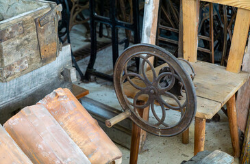 old cast iron crank and wooden machine parts, surrounded by vintage furniture and metal bases.