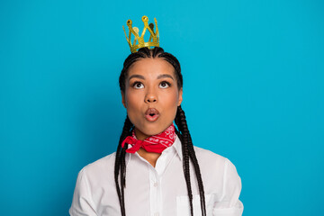 Stylish young woman wearing a small crown, red scarf, and white shirt, looking curious against a...