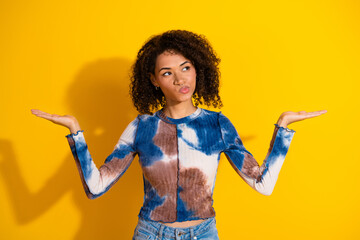 Young woman in tie-dye shirt with thoughtful expression posing against a vibrant yellow background