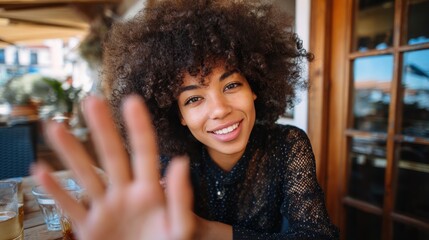 Pretty young African American mixed race hipster vlogger woman with Afro hair waving hand looking at webcam talking to camera sits at cafe table video calling, recording blog, headshot portrait., no 