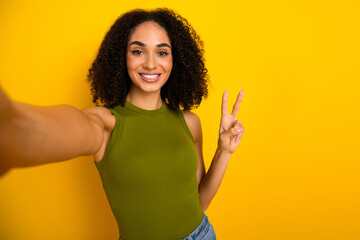 Cheerful young woman taking self-portrait selfie with peace hand gesture wearing casual green top...