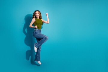 Joyful young woman posing against a blue background in stylish casual attire with a happy...