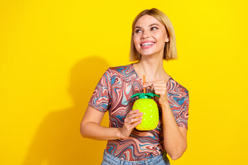 Happy young woman holding green decorative cup with yellow background showcasing leisure and style
