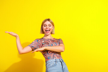 Joyful blonde woman in casual printed top posing playfully against a bright vibrant yellow...
