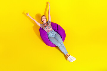 Young woman lounging stylishly on a purple bean bag against a vibrant yellow background enjoying...