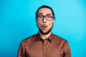 Young stylish man in brown shirt with a surprised expression against a teal background representing...